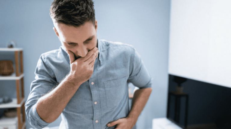 A gay person standing in a living room, appearing to be suffering from nausea and vomiting.