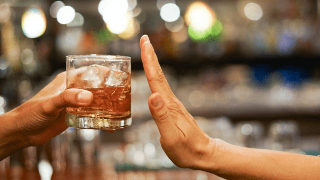 Close-up of two hands and a glass of alcohol, depicting the challenge of resisting temptation.