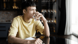 Portraying the signs of alcohol withdrawal is a gay guy looking contemplative while holding a glass of water.
