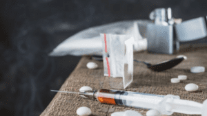 This is a picture of a used syringe, pills, and drug paraphernalia on a table.