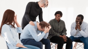 Support group session at a rehabilitation center, with a diverse group of individuals offering emotional support to a distressed gay man.