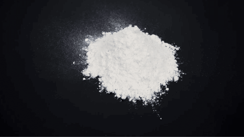 A close-up image of a white powder pile on a black surface, illustrating the drug cocaine or coke.