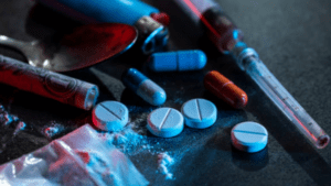 A mix of illegal drugs, pills, syringe, and a burnt spoon on surface.