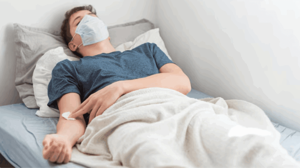 A masked gay man lying on a hospital bed.