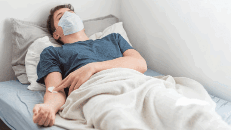 A masked gay man lying on a hospital bed.
