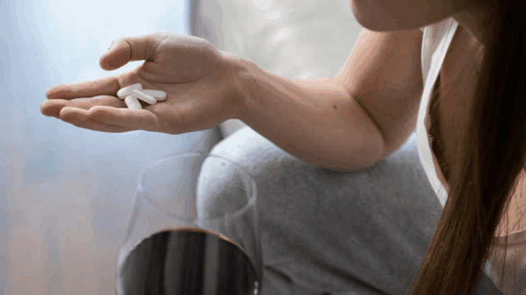 A trans person having benzo tablets on their palm while holding a glass of wine.