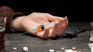 A hand of a person high on fentanyl while holding a syringe with fentanyl content on a table.