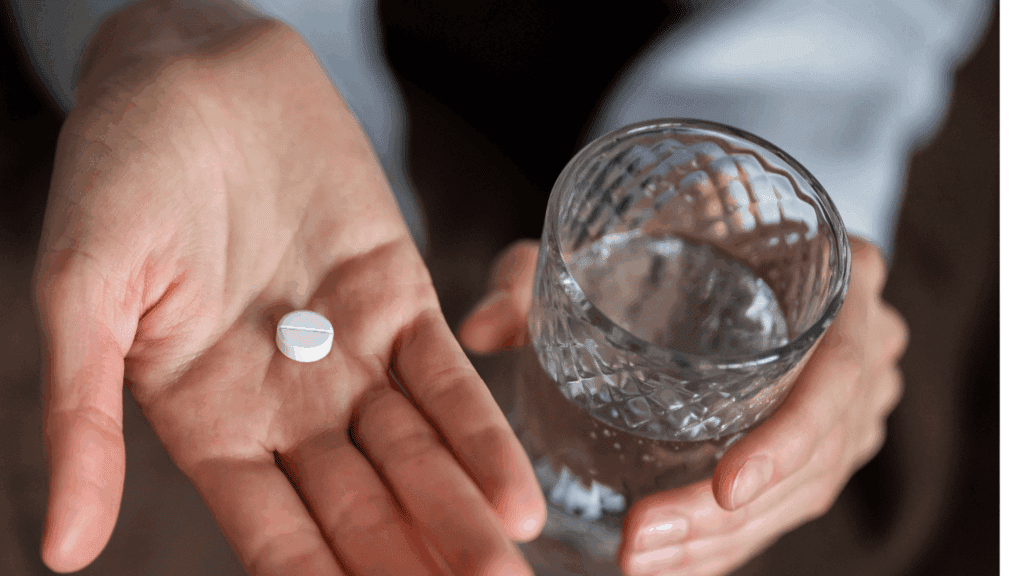 A hand holding a glass of water and a white naltrexone.