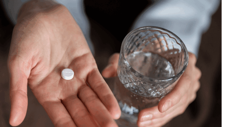 A hand holding a glass of water and a white naltrexone.