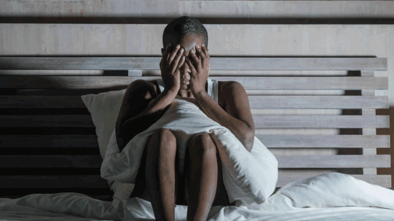 A black gay person sitting on a bed in sorrow during meth abuse treatment.