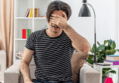 Distressed gay man sitting on a couch, possibly experiencing withdrawal symptoms like alcohol shakes in a home environment.