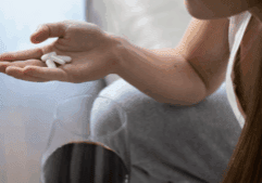 A trans person having benzo tablets on their palm while holding a glass of wine.