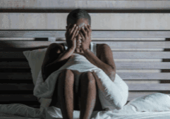 A black gay person sitting on a bed in sorrow during meth abuse treatment.