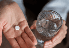 A hand holding a glass of water and a white naltrexone.